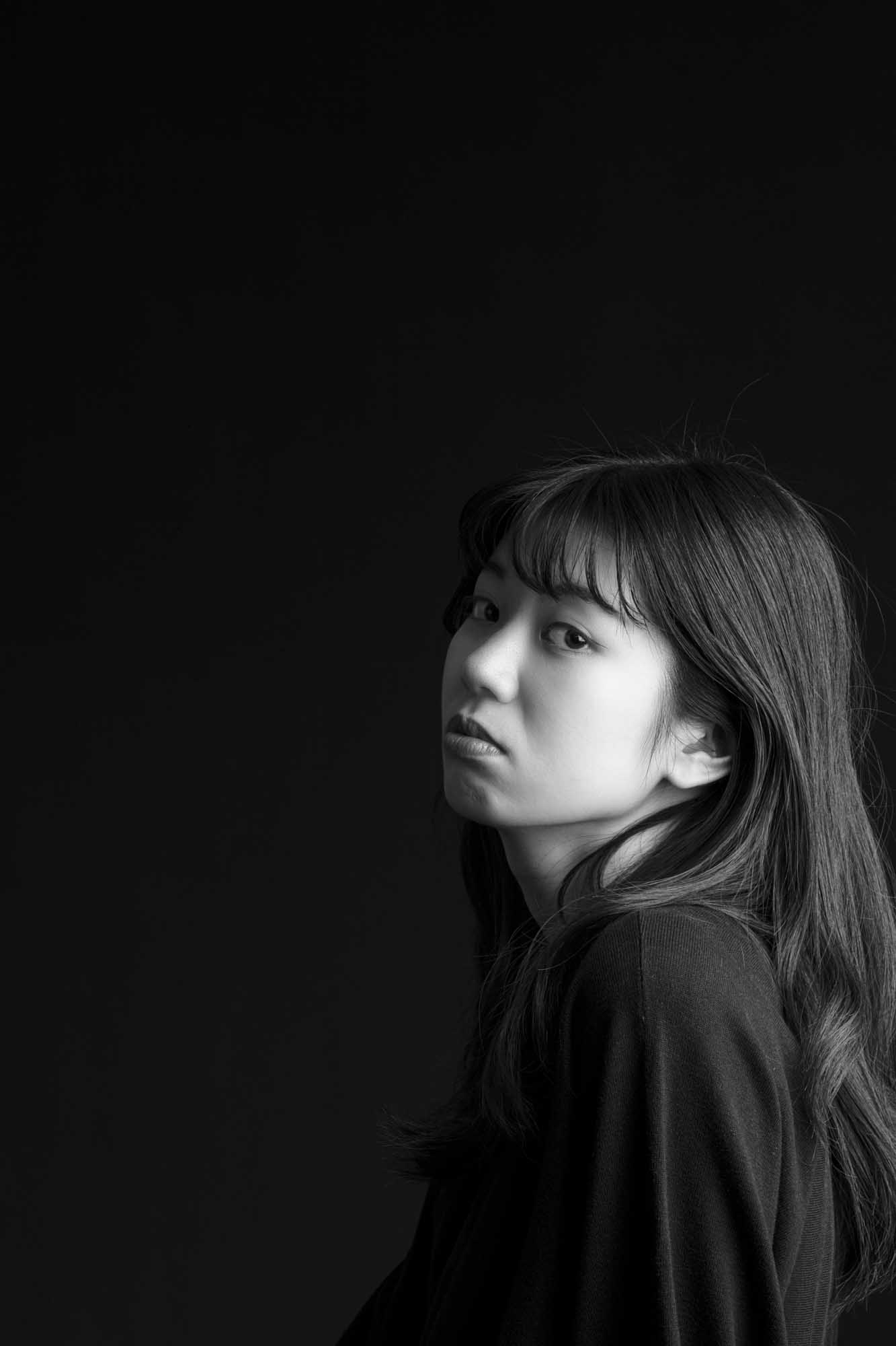 画像: 黒背景に撮影された女性の白黒ポートレート。横顔が強調され、シンプルでエレガントな印象を与えます。キーワード: ポートレート写真、白黒、