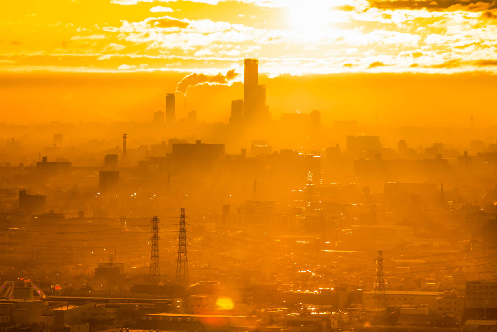 画像: この画像は、都市の夕焼けを背景にしたシルエットの街並みを描いています。空を黄金色に染める夕日がビル群を暖かく照らし、幻想的