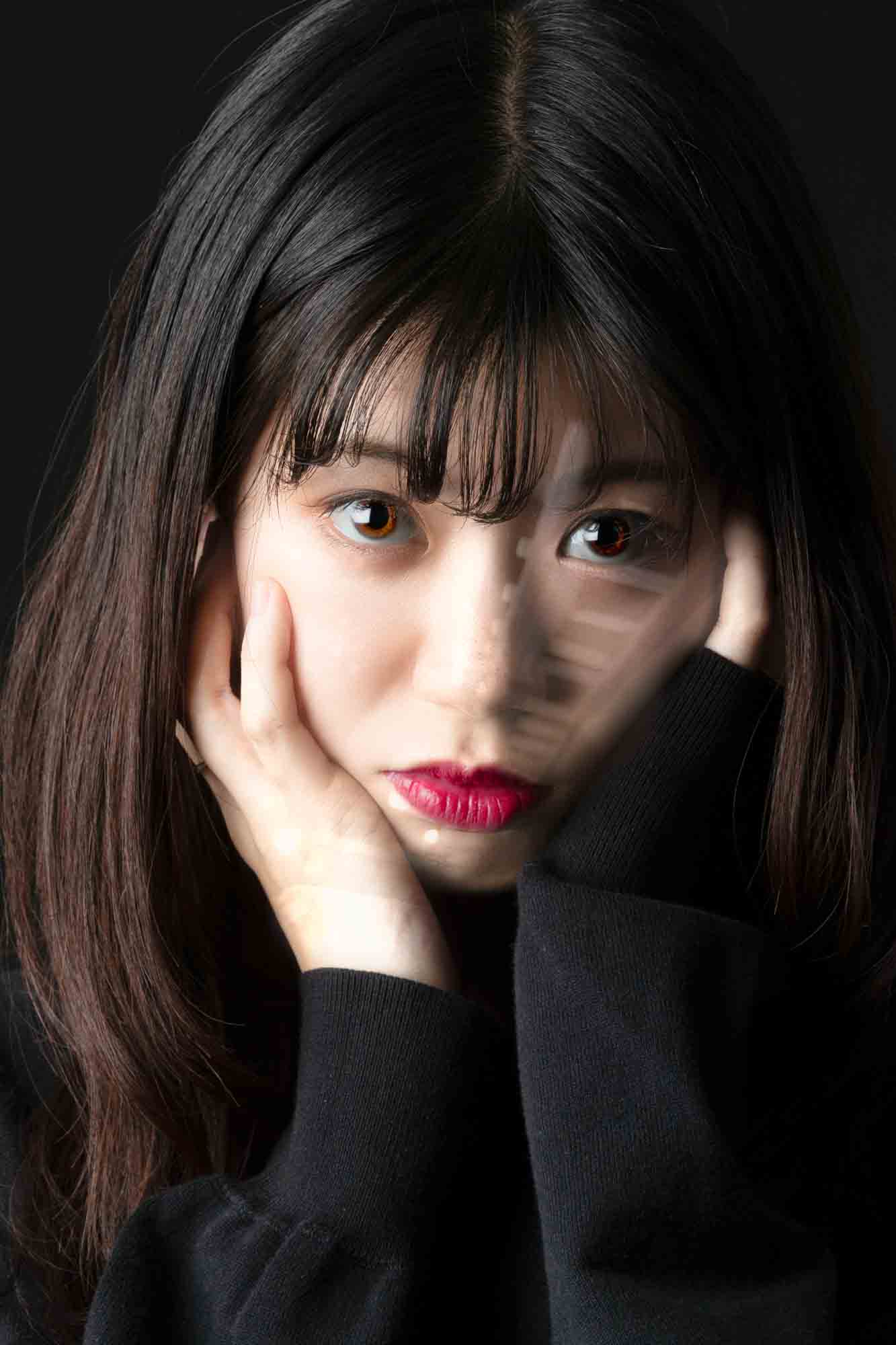 画像: 申し訳ありませんが、この画像に写っている人を識別することはできません。画像は若い女性が頬に手を添えてこちらを見つめているポートレートです。暗い背景と
