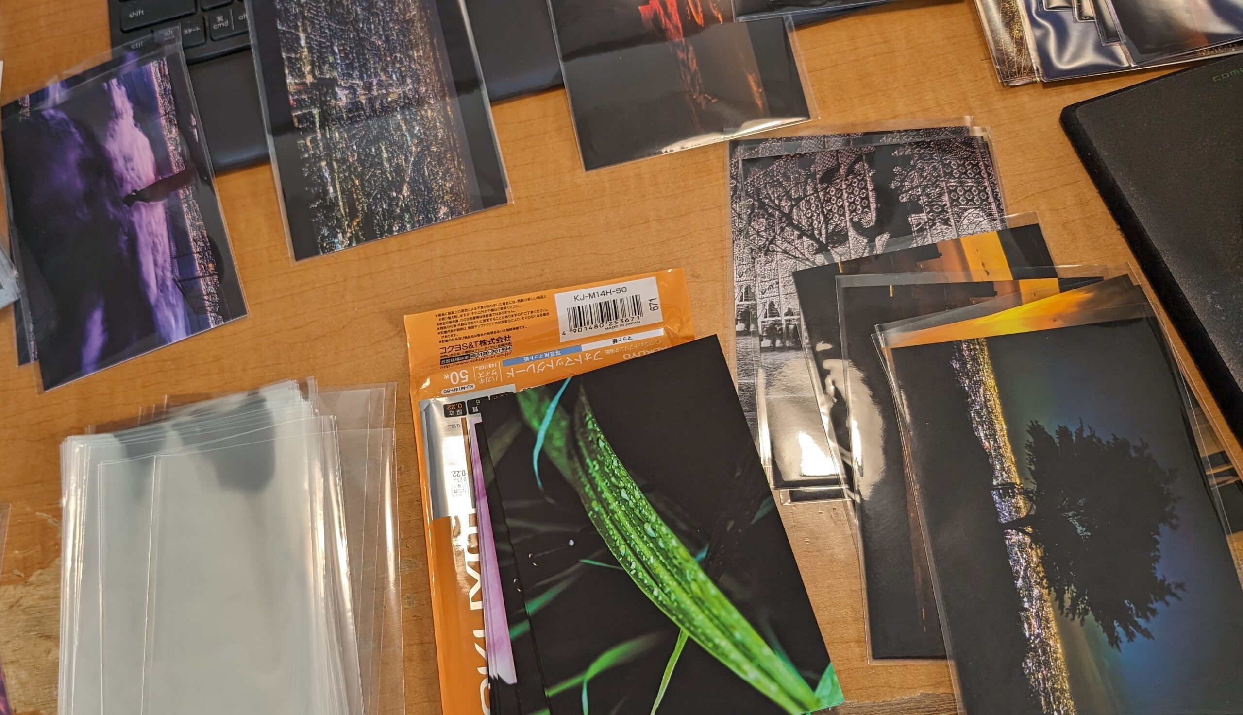 画像: 木製のテーブルに広げられたさまざまな写真が並んでいます。写真には自然の風景や夜景が含まれており、隣には写真用の透明な袋が置