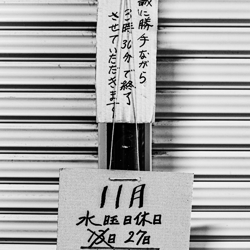 画像: 屋内のシャッターに貼られた営業に関する手書きの案内板。内容は、営業時間の変更や定休日に関する情報が記載されています。キーワード: 日本、営業時間、定休日