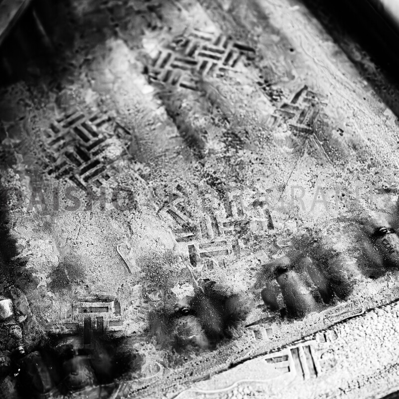 画像: この画像は、車の汚れた表面に付いたタイヤ跡です。白黒の色調が施され、滑らかで膜状の汚れが特徴的です。 キーワード: 車の